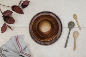 Nested acacia wooden bowls, wooden serving plate and wooden spoons from Vietnam arranged with natural leaves, representing EUDR and FSC deforestation-free sourcing