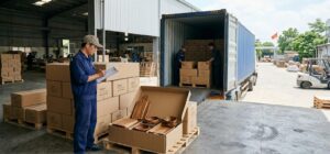 Export cartons of Vietnamese acacia wooden kitchenware on pallets being loaded into a 40ft container while a worker checks the packing list, illustrating FOB price and landed cost for 2026 buyers